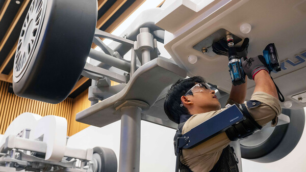 ▲'웨어러블 로봇 테크데이'에서 상완 근력을 보조하는 '엑스블 숄더' 로봇을 착용한 로보틱스랩 연구원이 팔을 올려 모형 차량 하부의 부품을 체결하는 모습.